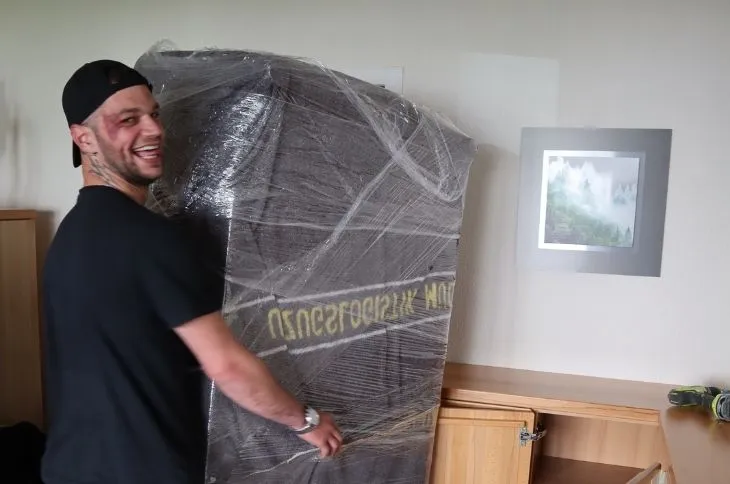 gluecklicher umzugshelfer traegt verpacktes moebel im wohnraum